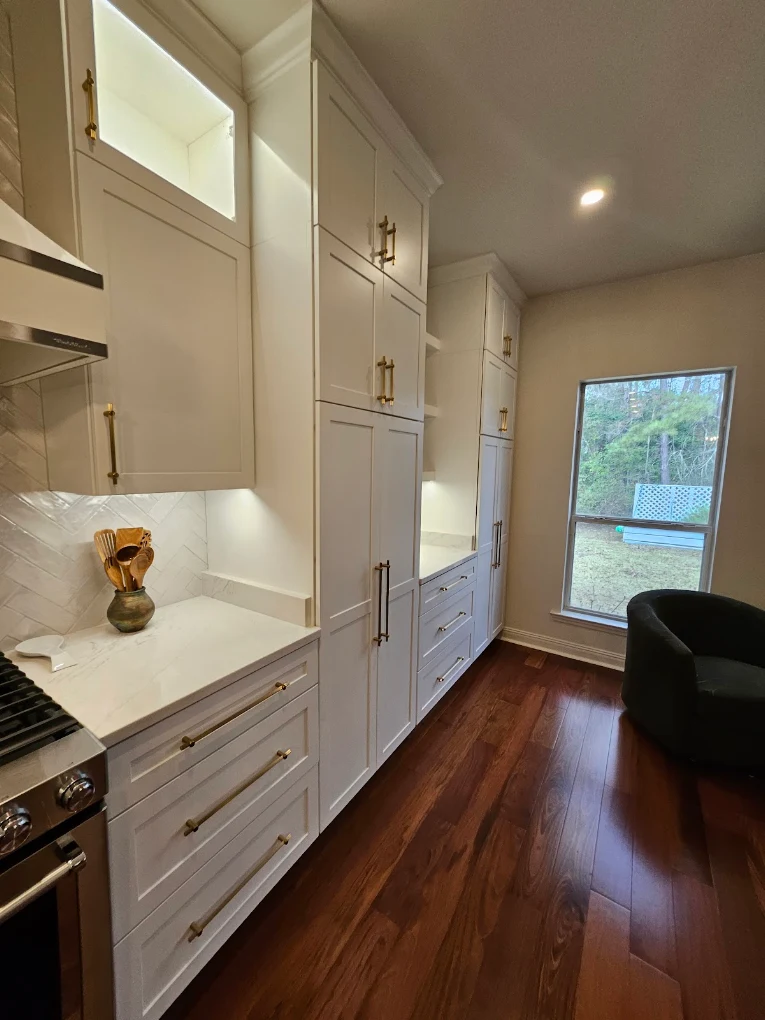 White kitchen cabinets with brass handles, upper windows, and wood flooring