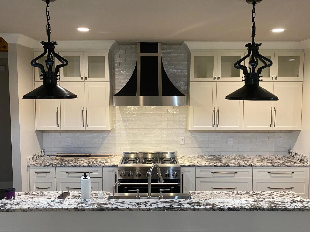 White kitchen cabinets with granite countertops, a stainless steel range hood, and black pendant lights