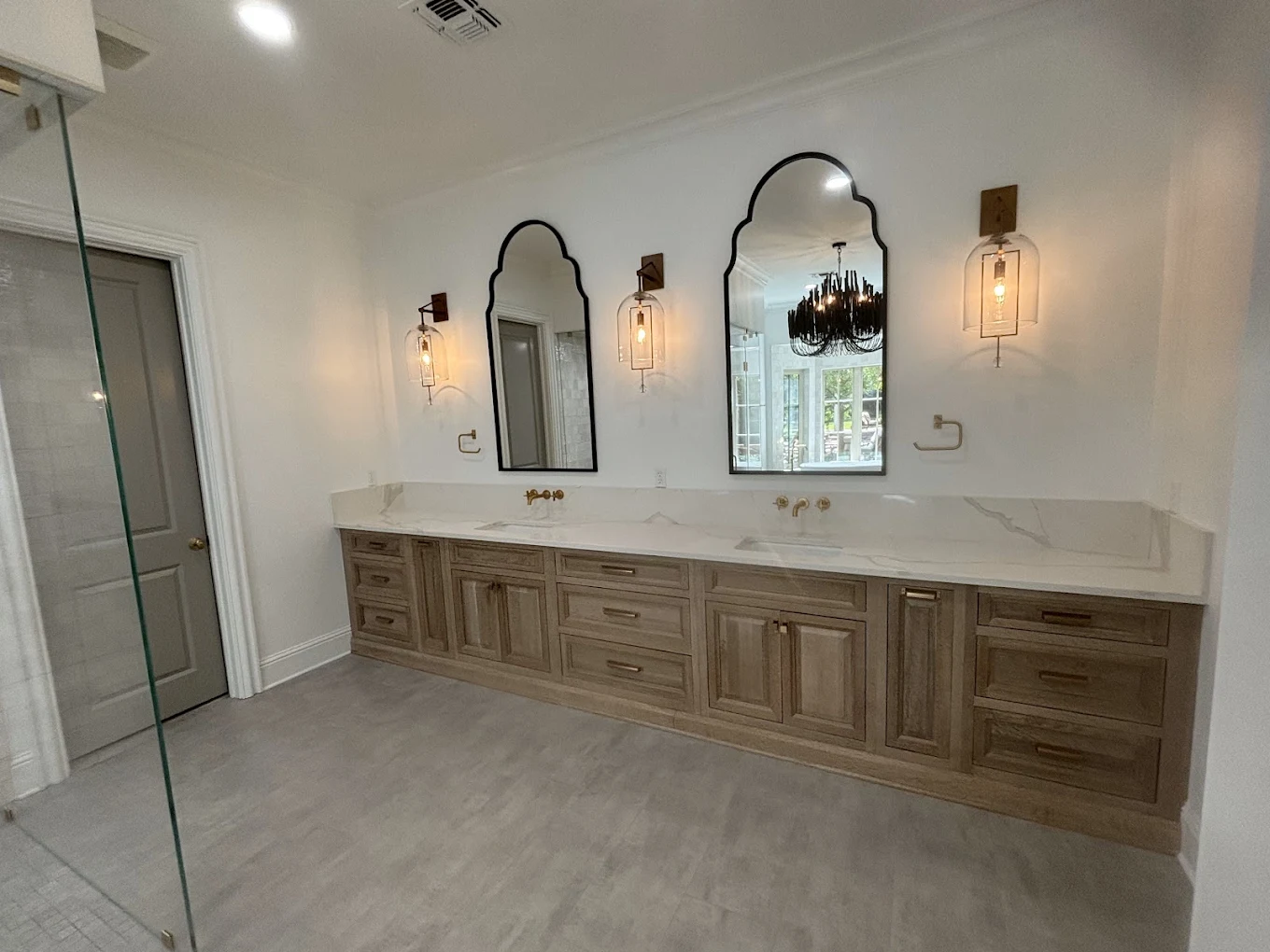Wood bathroom vanity with two arched mirrors, wall sconces, and a white countertop