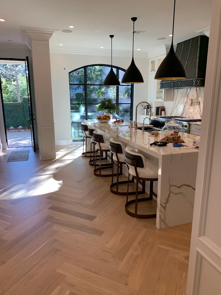 Kitchen with a white waterfall island, bar stools, black pendant lights, and herringbone wood flooring
